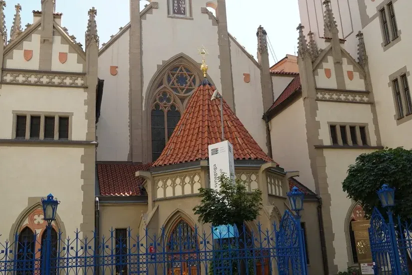 Vista exterior de la Sinagoga Pinkas en Praga con una Estrella de David dorada en su tejado y una valla azul ornamentada.