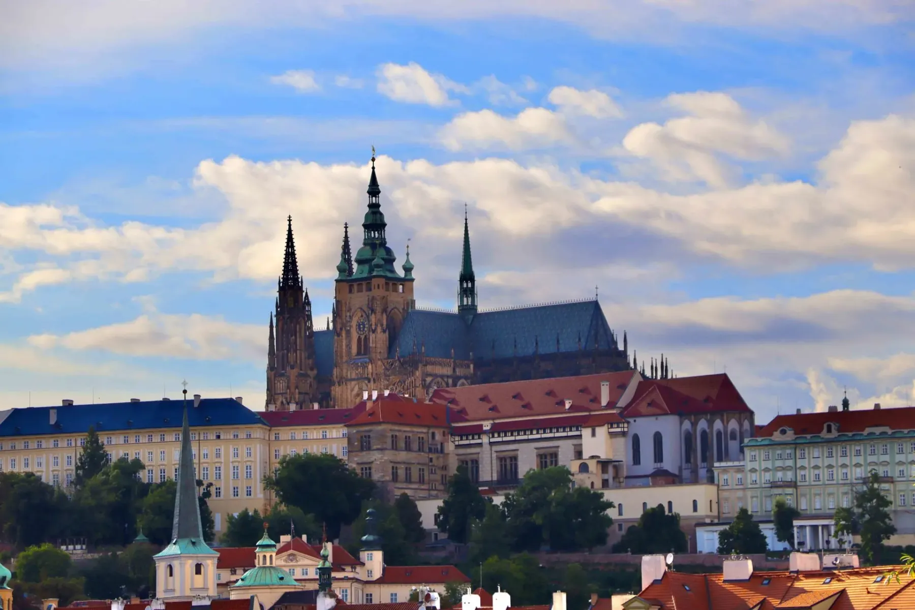 Catedral de San Vito y el complejo del Castillo de Praga sobre edificios de la ciudad bajo un cielo parcialmente nublado.