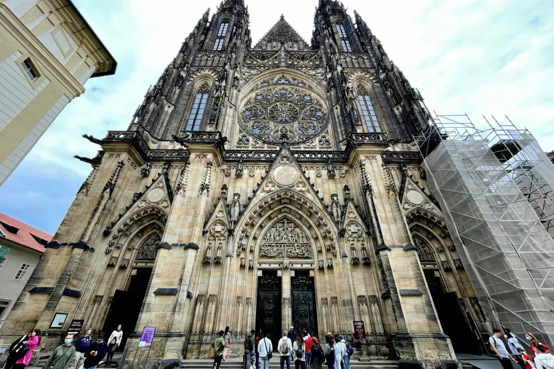 Fachada de la Catedral de San Vito en Praga, mostrando arquitectura gótica, rosetón, torres gemelas y personas. Andamios v...