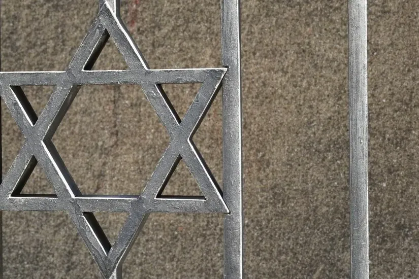 Valla metálica con una Estrella de David en el centro, sobre una pared gris texturizada.