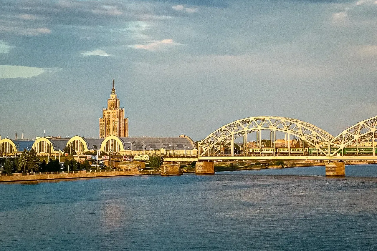 Blick über die Daugava in Riga: Eisenbahnbrücke mit grünem Zug, Gebäude des Zentralmarktes und die Lettische Akademie der ...