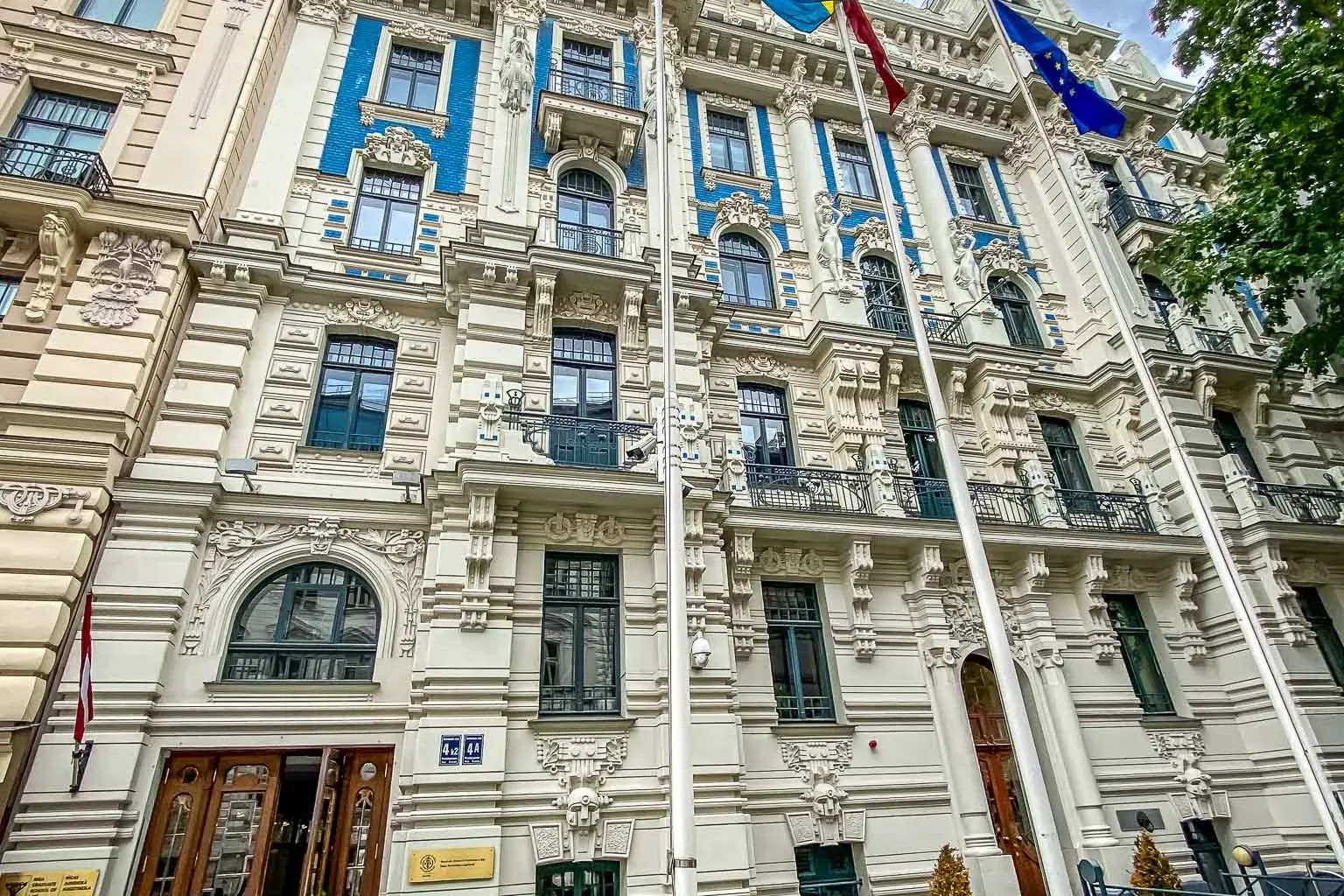 Verziertes Jugendstilgebäude in Riga mit cremefarbener Fassade, blauen Details, dunklen Fenstern und Flaggen Schwedens und...
