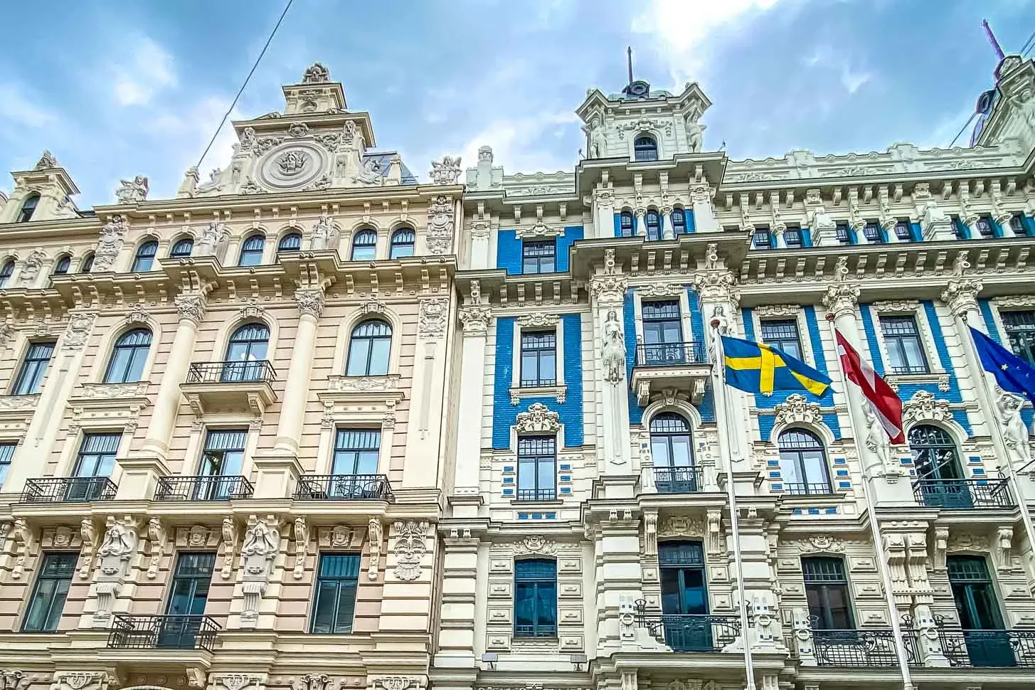 Verzierte Jugendstilgebäude in Riga mit detailreichen Fassaden, Balkonen und Flaggen Lettlands, Schwedens und der EU.