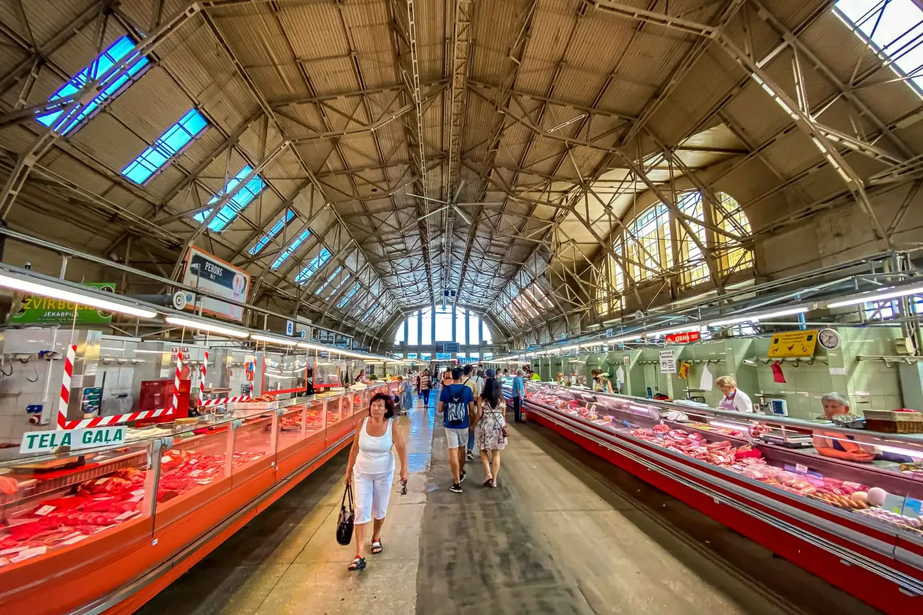 Innenansicht der Fleischhalle des Rigaer Zentralmarktes, mit langen Kühltheken voller frischem Fleisch und Kunden.