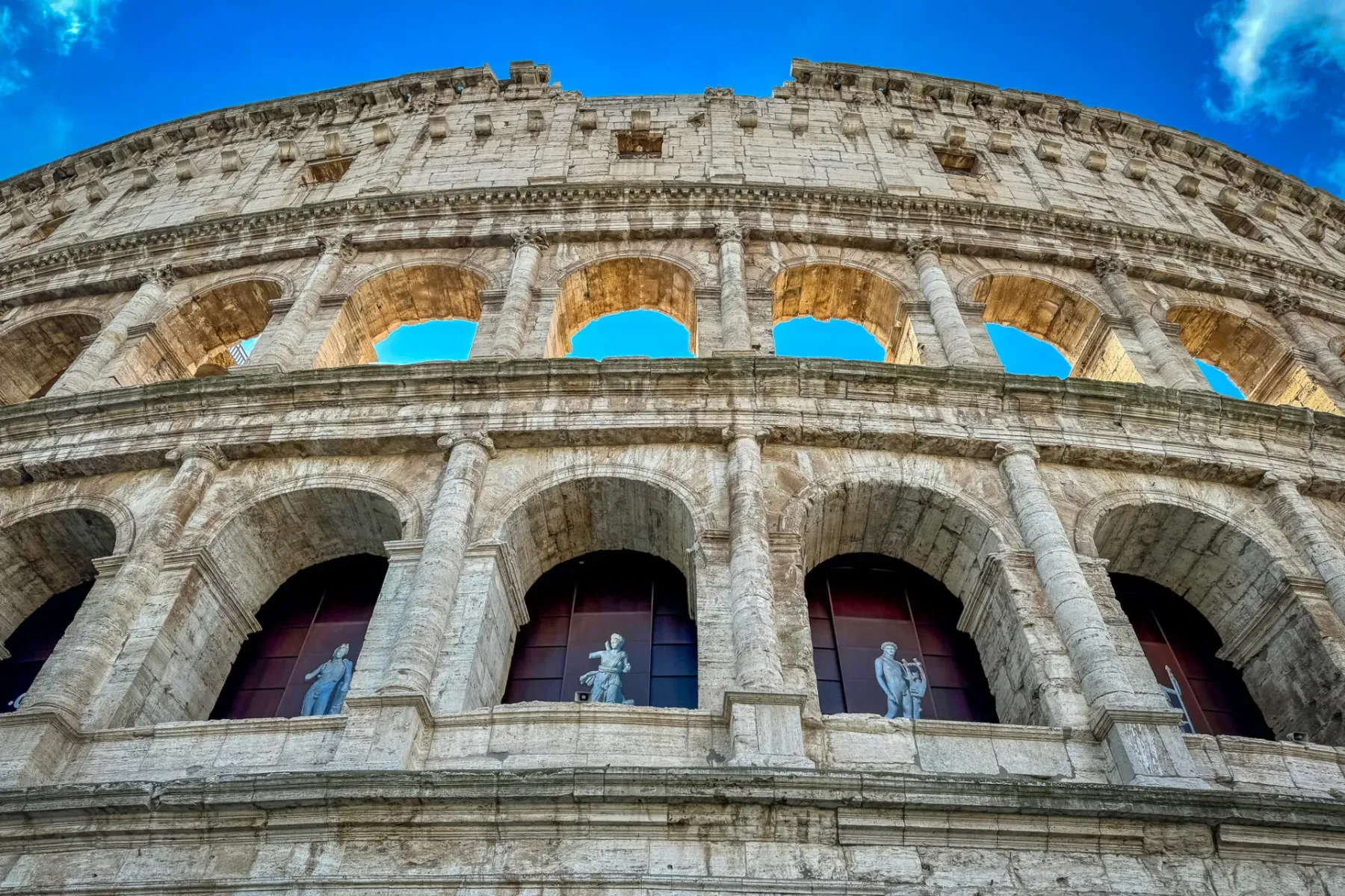 Vista de ángulo bajo del Coliseo en Roma, mostrando su impresionante arquitectura y estatuas.