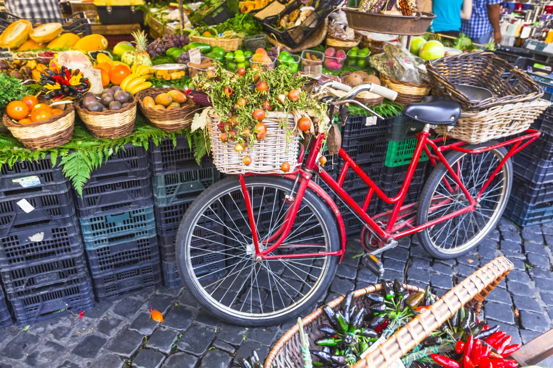 Rotes Fahrrad mit einem Korb voller kleiner Granatäpfel neben einem Marktstand mit frischem Obst und Gemüse auf Kopfsteinp...