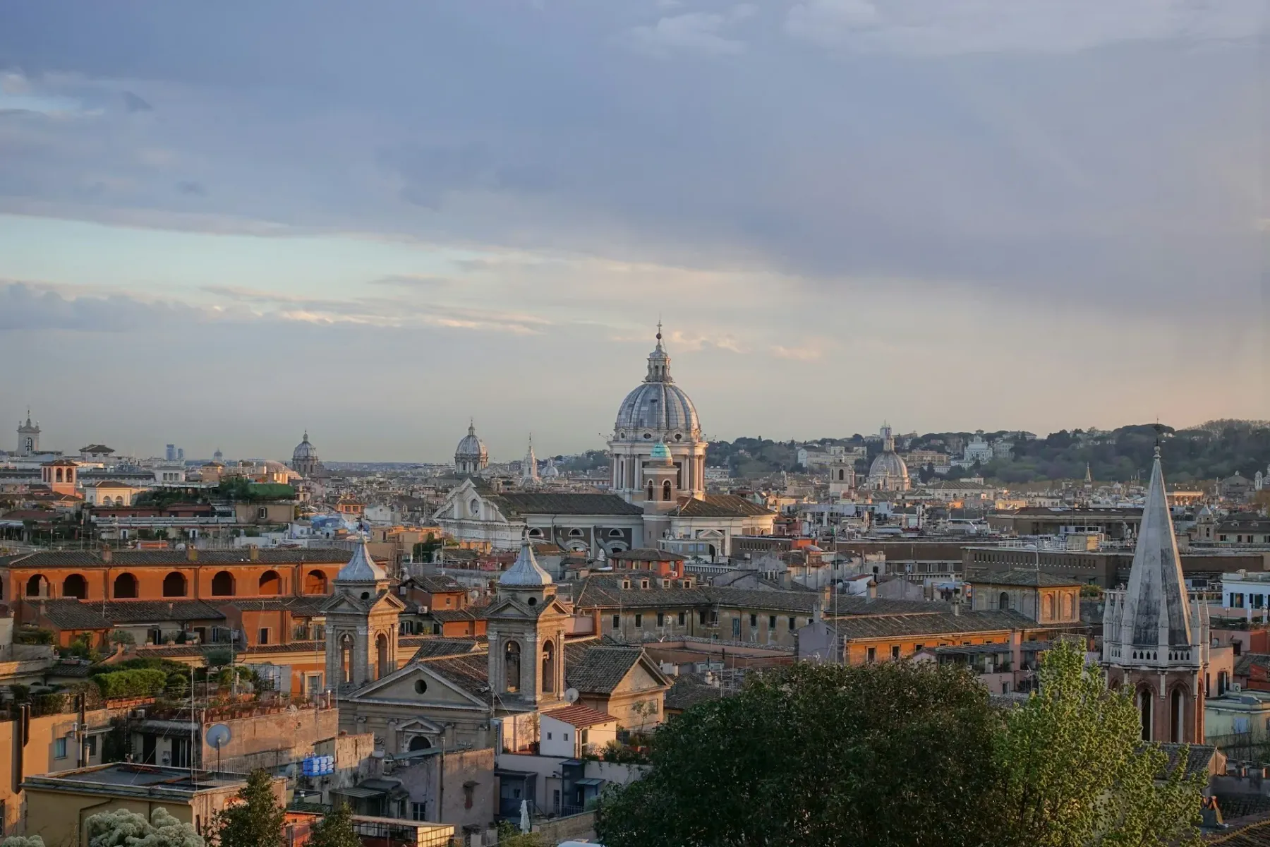 Panoramablick auf Rom bei Sonnenuntergang mit mehreren Kirchenkuppeln und Terrakottadächern unter einem sanften, bewölkten...