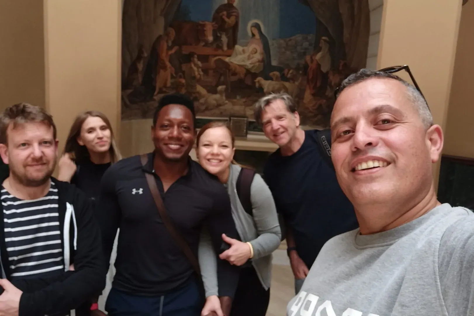 Turistas felices en una visita guiada en Roma, posando para una selfie frente a una pintura de la Natividad.
