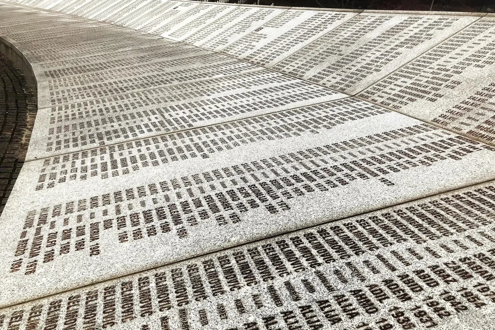 A curved memorial wall inscribed with numerous names and dates.
