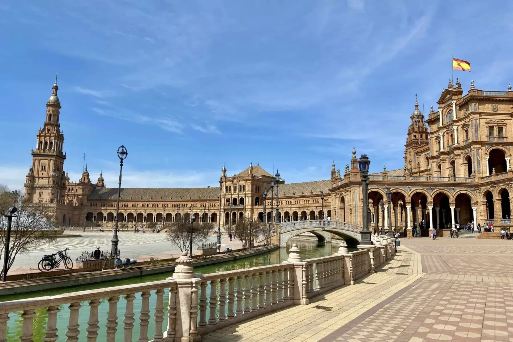 Widok na Plaza de España w Sewilli: budynek z wieżą, kanał z mostem i ozdobna balustrada.