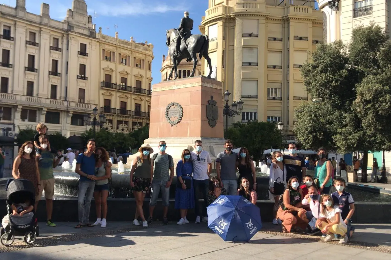 People on a walking tour posing in a sunny city square with an equestrian statue, a fountain, and historic buildings.