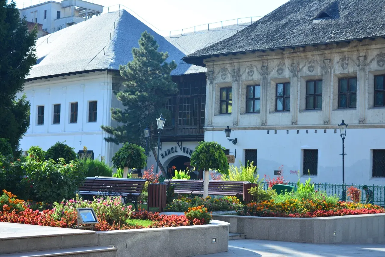Edificios históricos con tejados texturizados y un patio ajardinado con coloridos parterres, bancos y árboles.