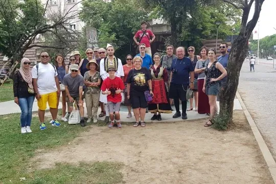 Eine vielfältige Gruppe von Touristen, teilweise in traditioneller albanischer Kleidung, posiert an einem sonnigen Tag in ...