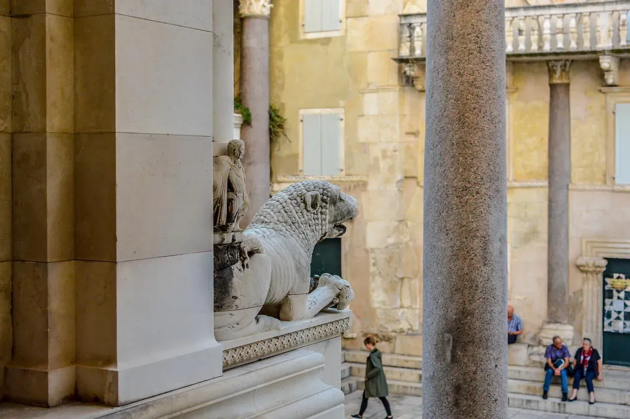 Estatua de león de piedra tallada sobre un pedestal, parcialmente oculta por una columna, en un palacio antiguo en Split.