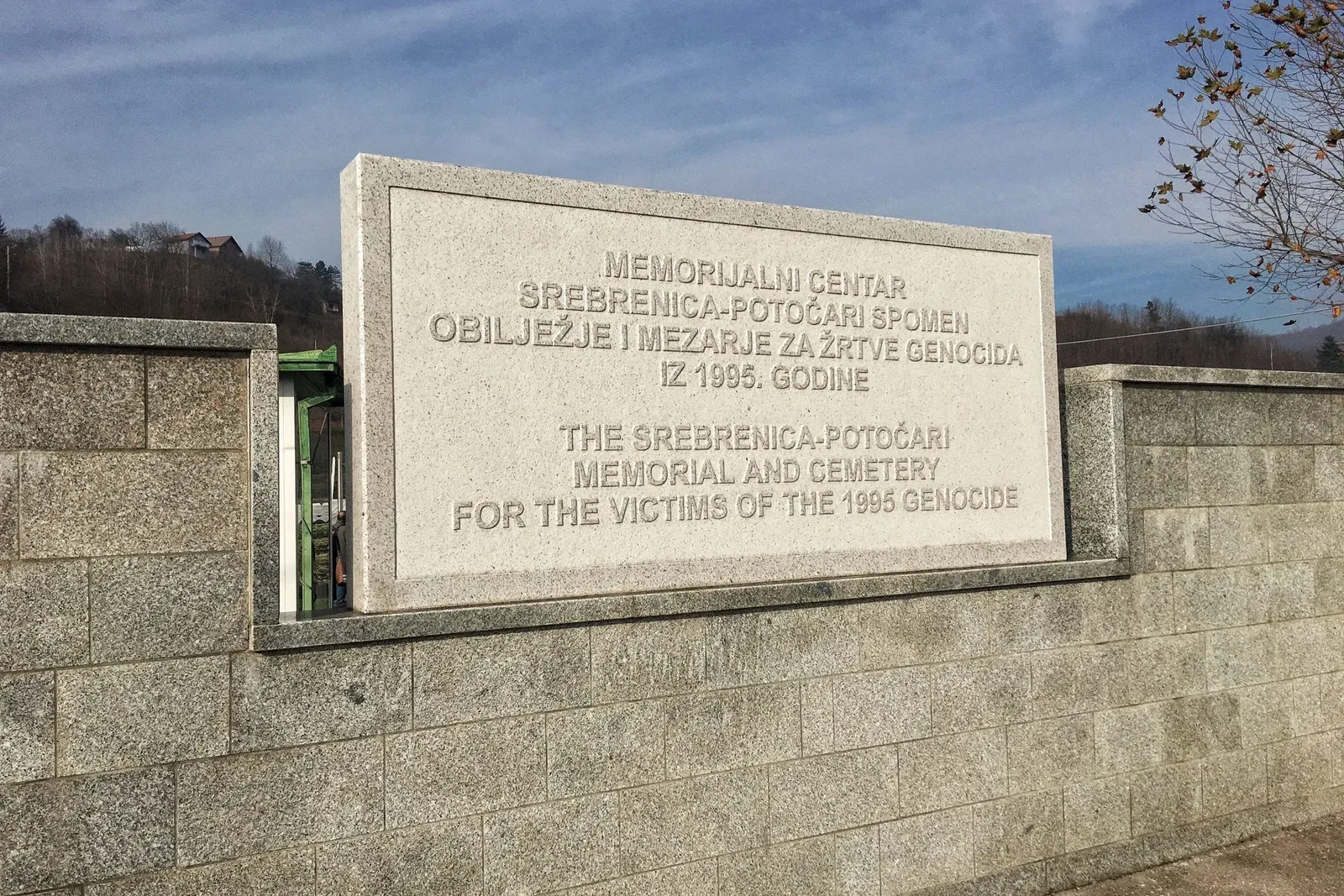 Stone monument with text in Bosnian and English: 'Srebrenica-Potočari Memorial and Cemetery for the victims of the 1995 Ge...
