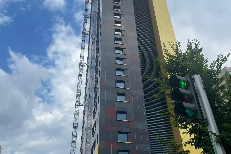 Wysoki, nowoczesny budynek w budowie z ciemno-złotą elewacją, dużym żurawiem i zielonym światłem w Tiranie.