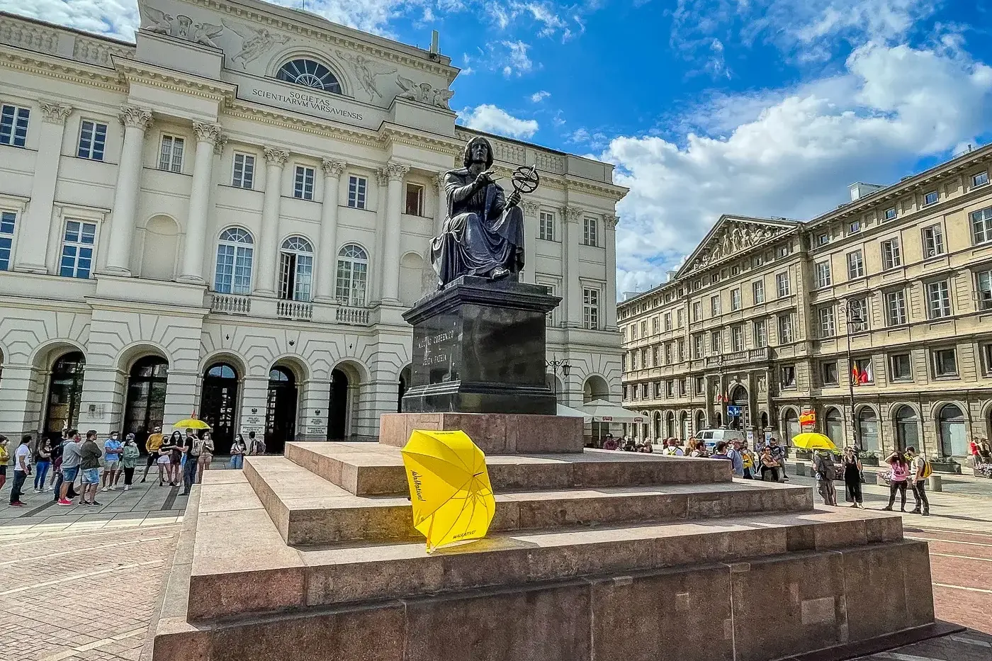 Estatua de bronce de Nicolás Copérnico con esfera armilar frente al Palacio Staszic en Varsovia, bajo cielo azul.