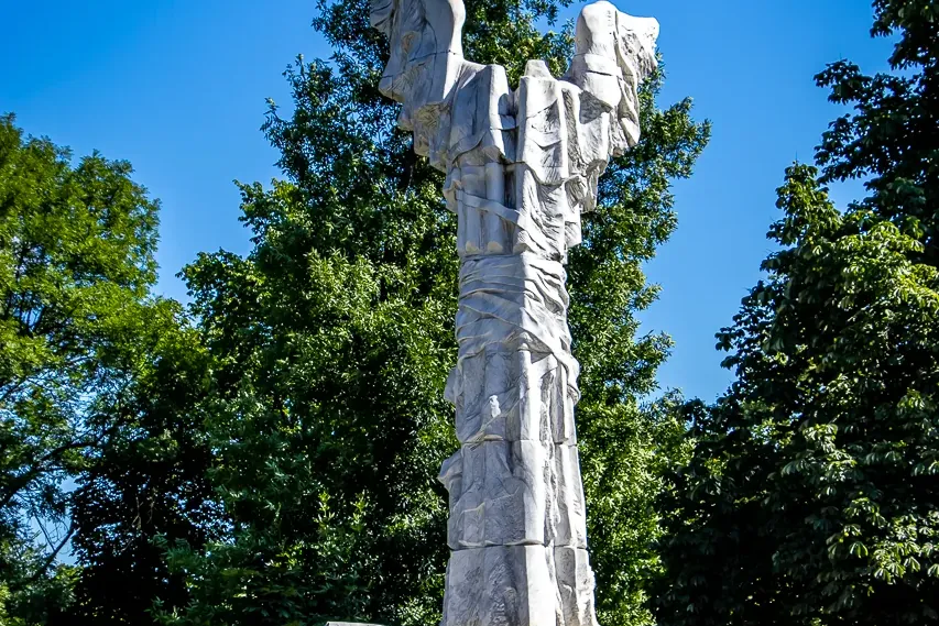 Wysoki, jasny pomnik z kamienia poświęcony Monte Cassino, z orłem i napisem 'MAJ 1944' na podstawie, na tle nieba i drzew.