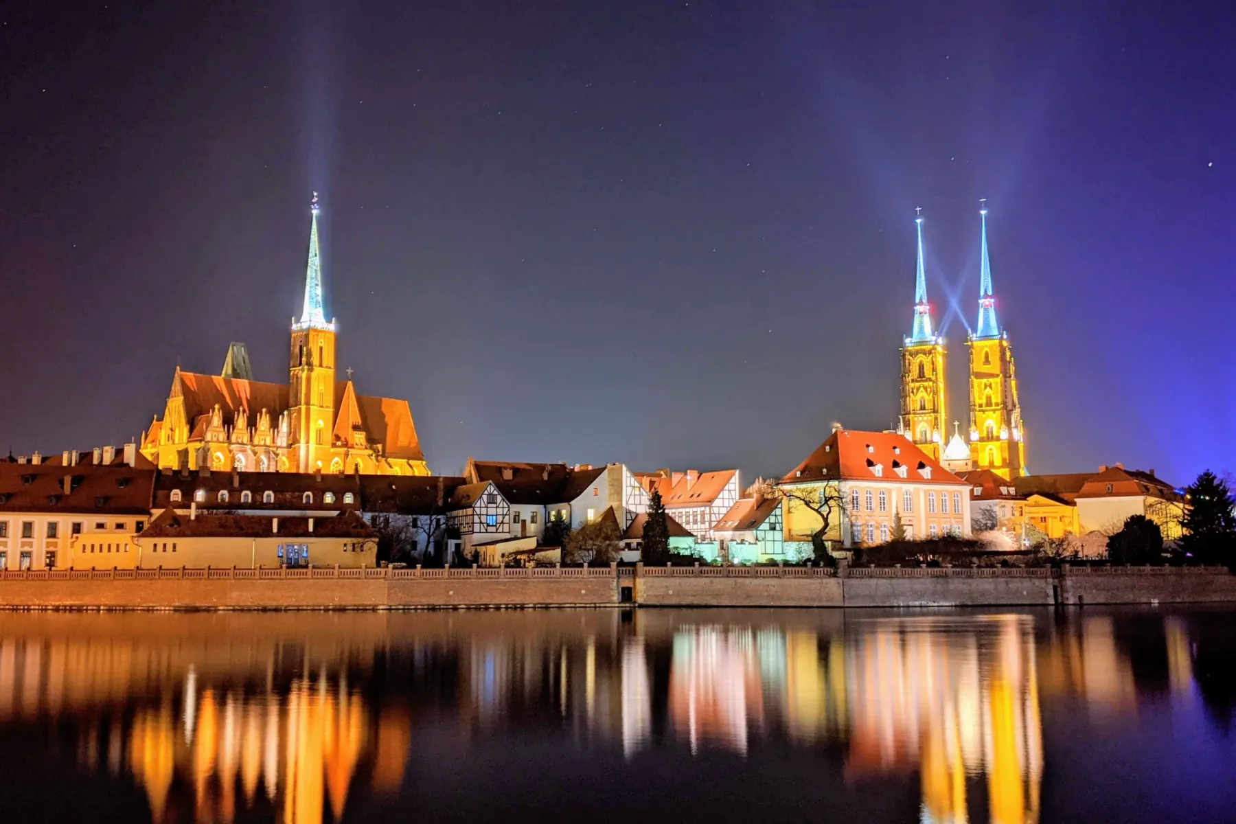 Nocny widok Wyspy Katedralnej we Wrocławiu, odbijającej się w rzece Odrze.