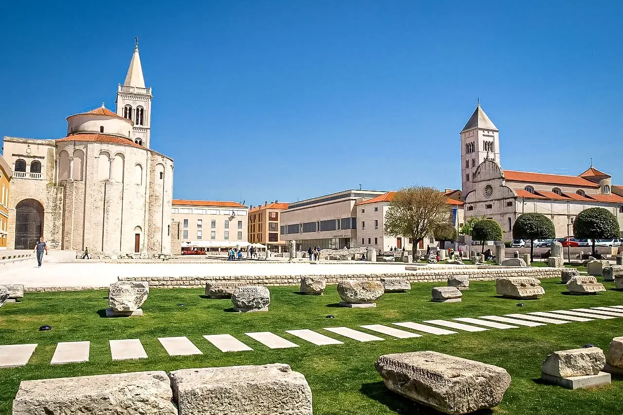 Ruinas del Foro Romano de Zadar con césped y bloques de piedra. Al fondo, la Iglesia de San Donato y la Catedral de Santa ...