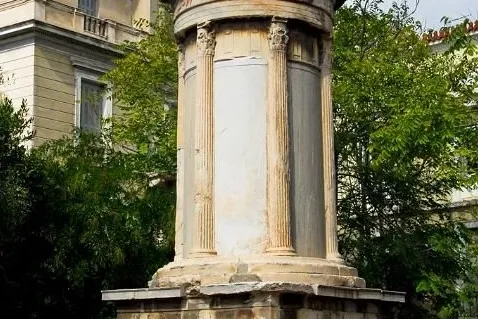 The Choragic Monument of Lysicrates, an ancient monument with Corinthian columns, surrounded by trees and buildings in Ath...