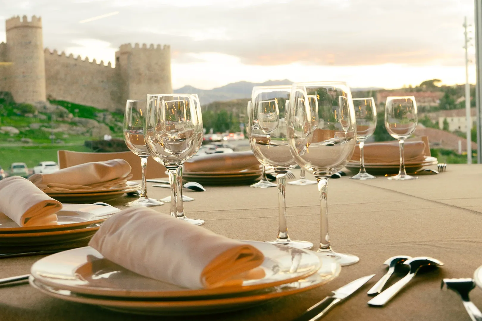 Ein gedeckter Esstisch mit Gläsern und Tellern, mit Blick auf die mittelalterlichen Stadtmauern von Ávila, Spanien, bei So...