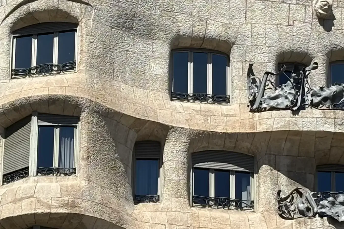 Detalle de la fachada ondulada de piedra de la Casa Milà con ventanas oscuras, persianas grises y balcones de hierro forjado.