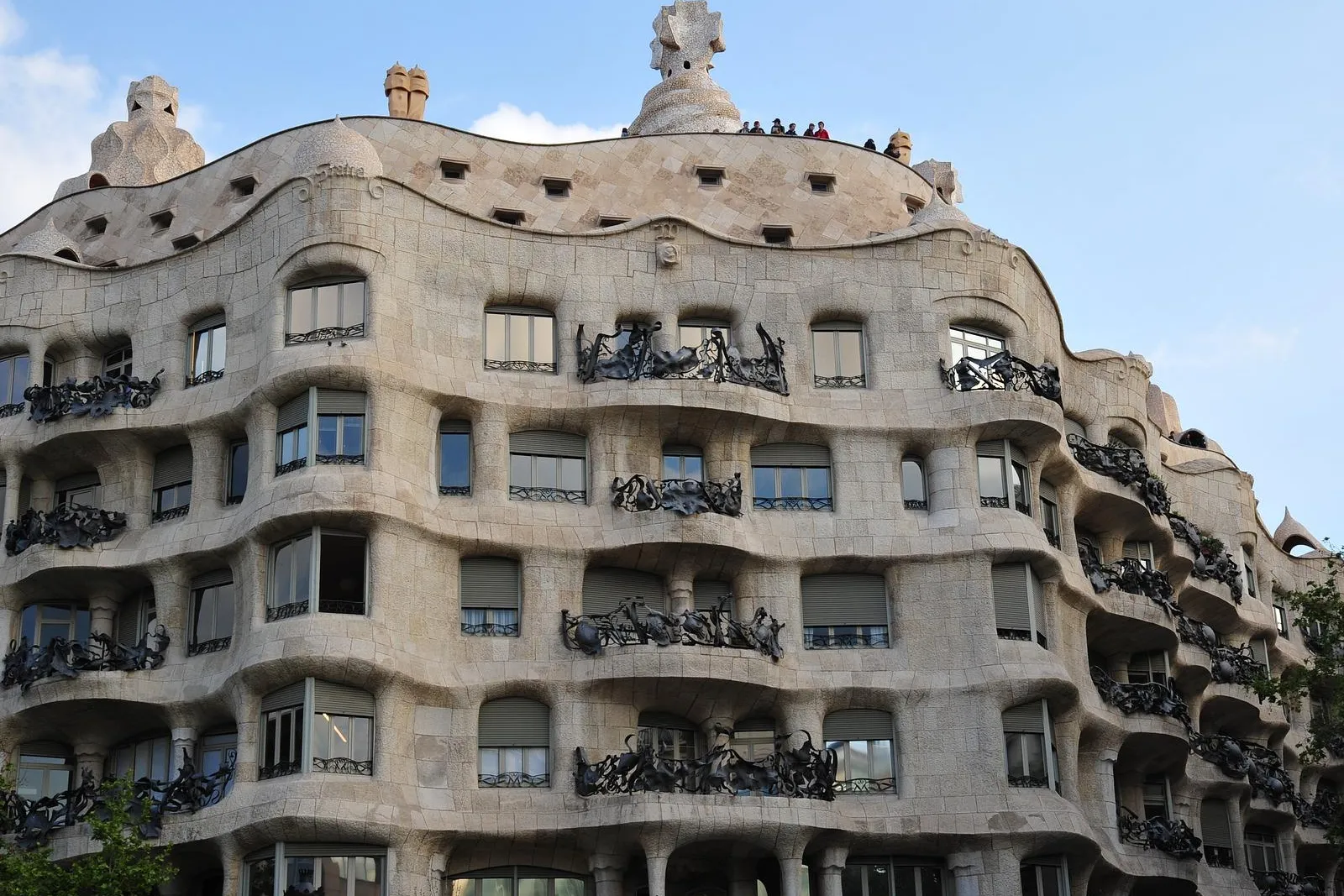 Geschwungene Steinfassade der Casa Milà (La Pedrera) mit kunstvollen Eisenbalkonen unter blauem Himmel, entworfen von Gaudí.
