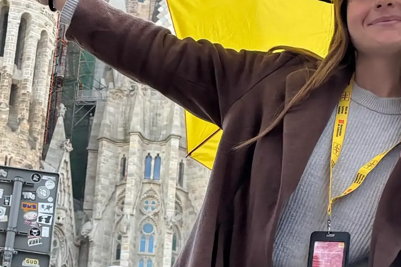 A smiling Walkative guide with a yellow umbrella in front of the Sagrada Familia in Barcelona, with its towers under const...
