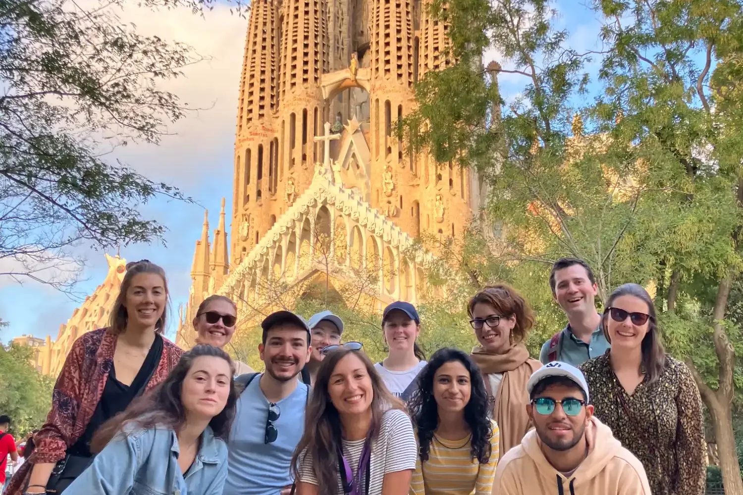Grupa uśmiechniętych turystów na wycieczce pozuje do zdjęcia przed bazyliką Sagrada Familia Gaudiego w Barcelonie.