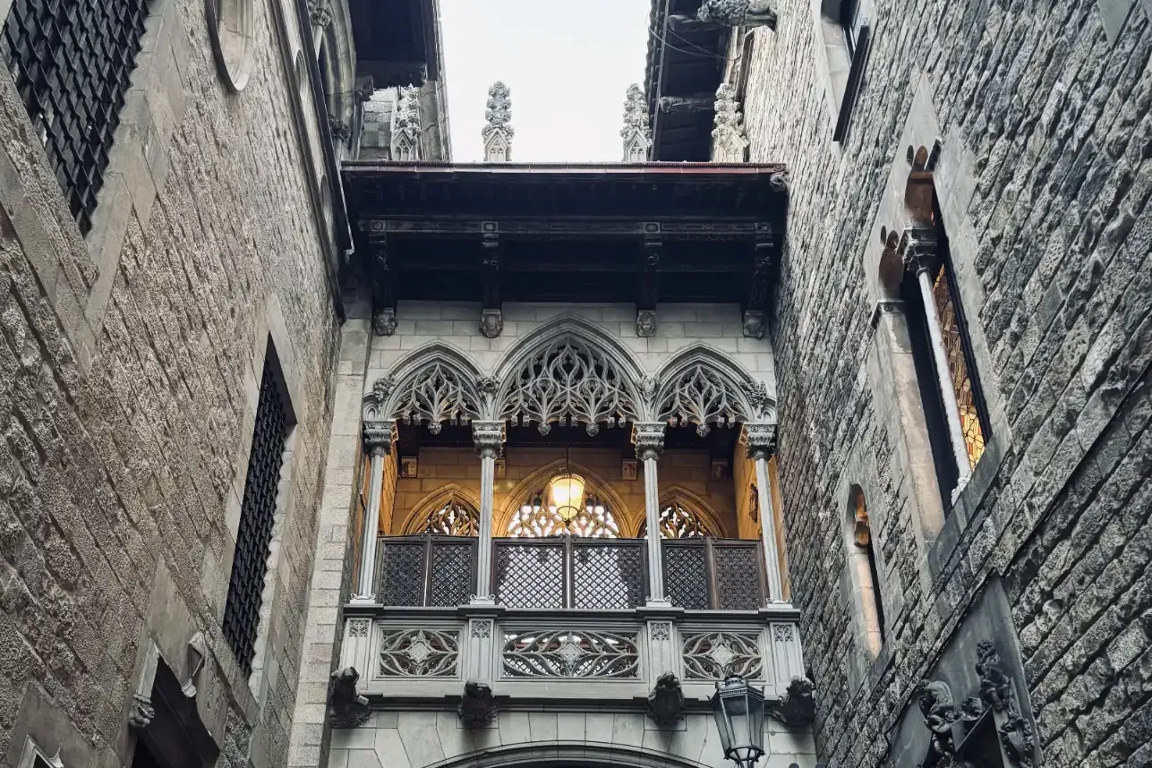 Puente neogótico de piedra ornamentado con farol y arco, que conecta dos edificios en un callejón estrecho.
