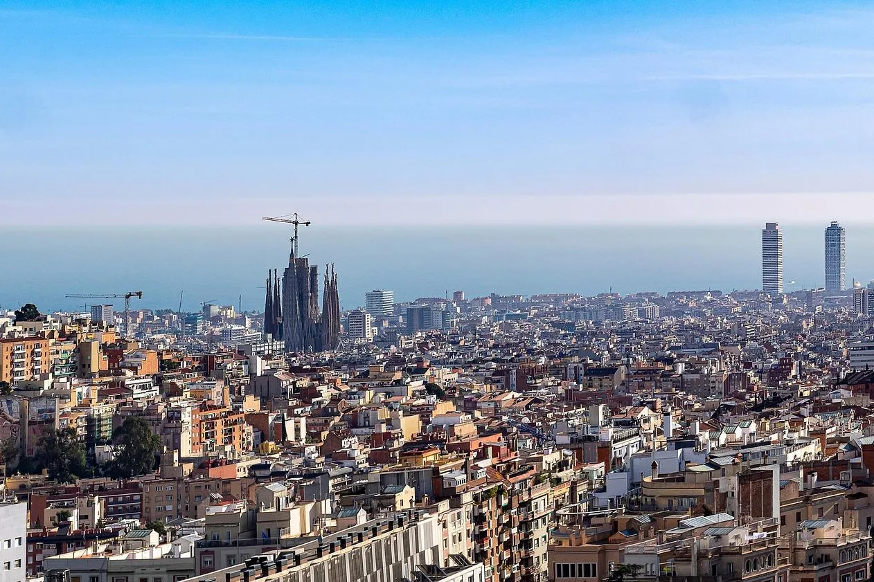 Panoramablick auf Barcelona mit der Sagrada Familia im Bau, dem Agbar Tower und zwei Wolkenkratzern am Meer.