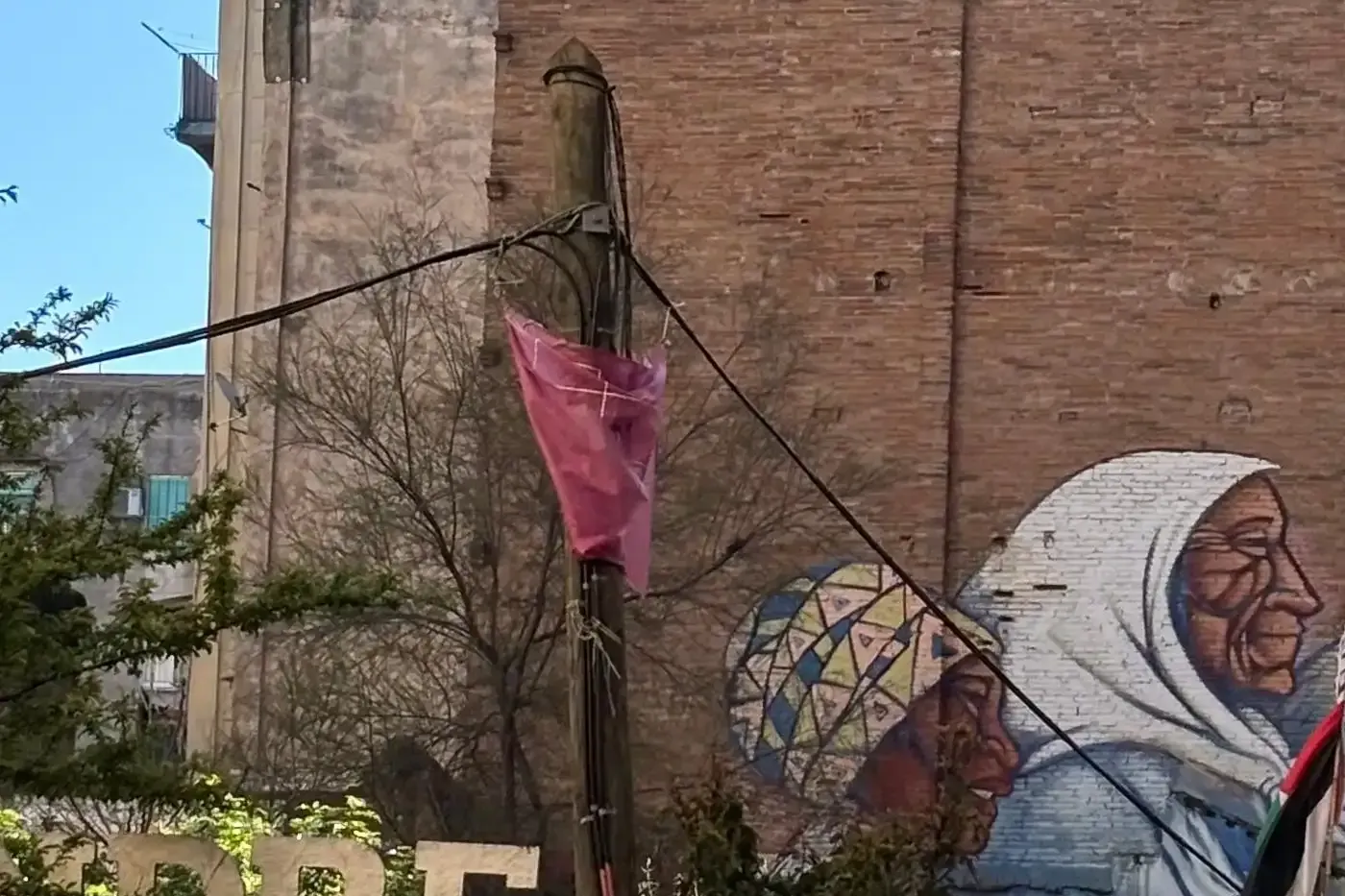 Mural of a young woman in a patterned headscarf on an orange wall, and older women murals on a brick building in Barcelona.