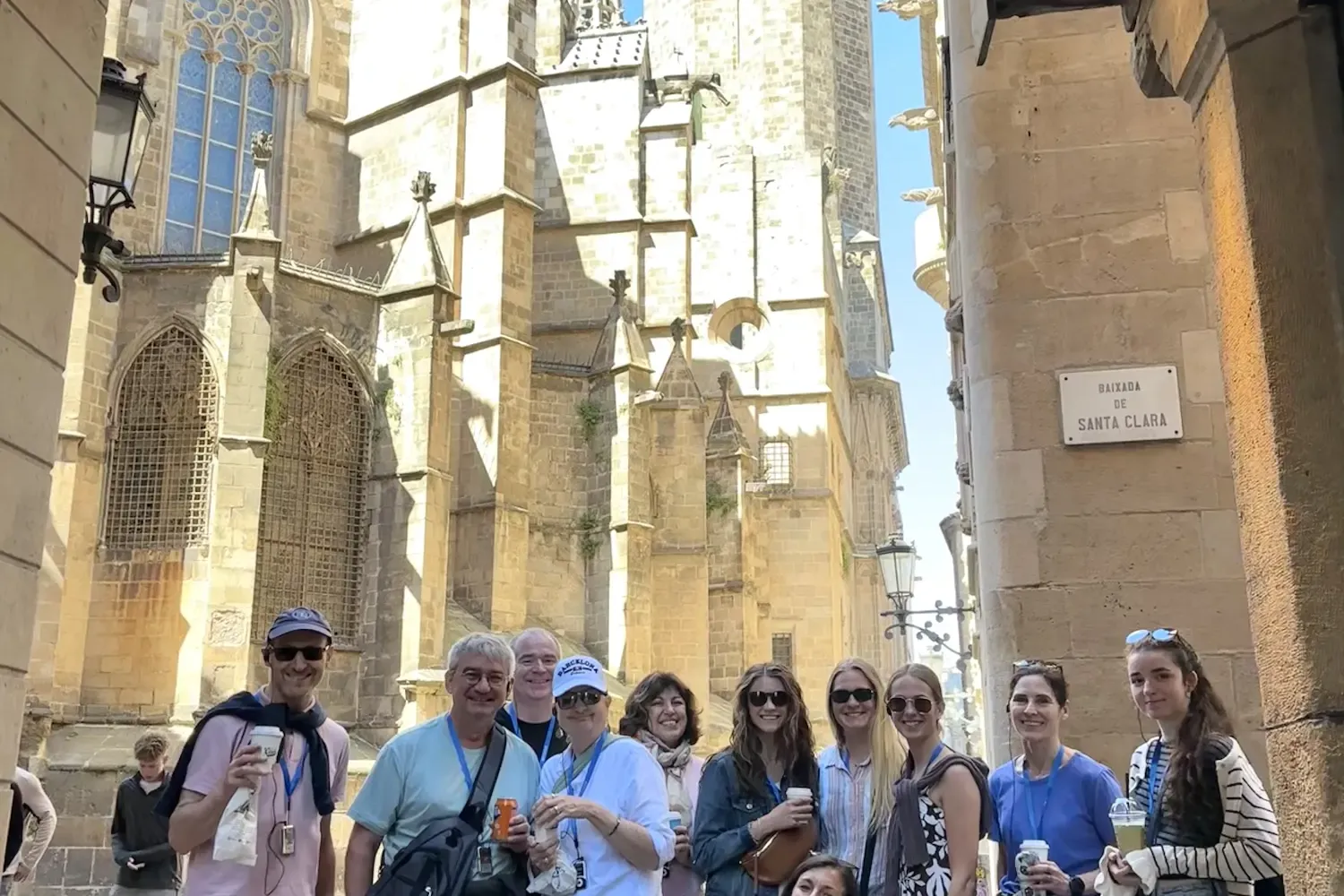 Un grupo diverso de personas de pie en una calle estrecha de piedra con la Catedral de Barcelona de fondo bajo un cielo azul.