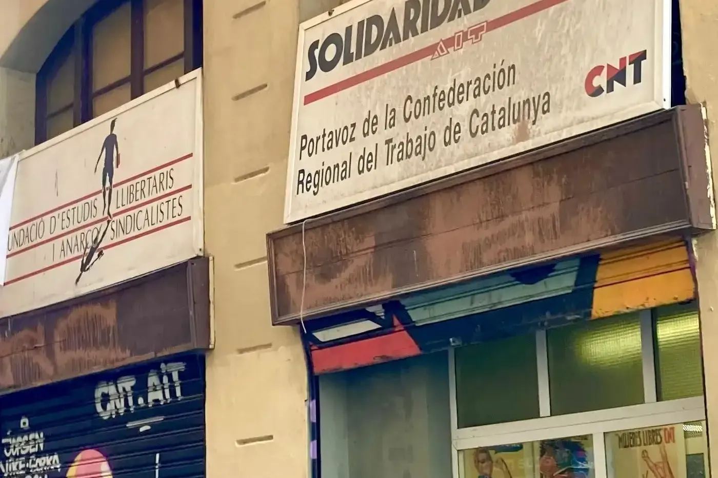Un grupo de personas en un tour urbano mirando hacia un edificio con letreros de "Solidaridad Obrera" y "CNT" y grafitis.