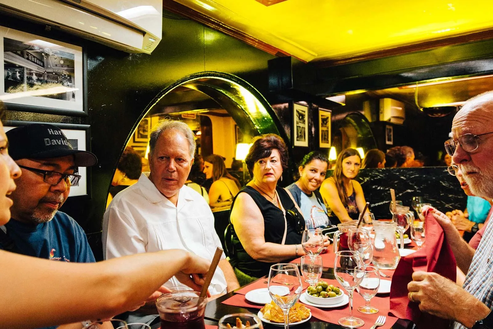 Eine Gruppe von Personen sitzt an einem Restauranttisch mit roten Tischdecken, teilt Tapas, Oliven und einen Krug Sangria.
