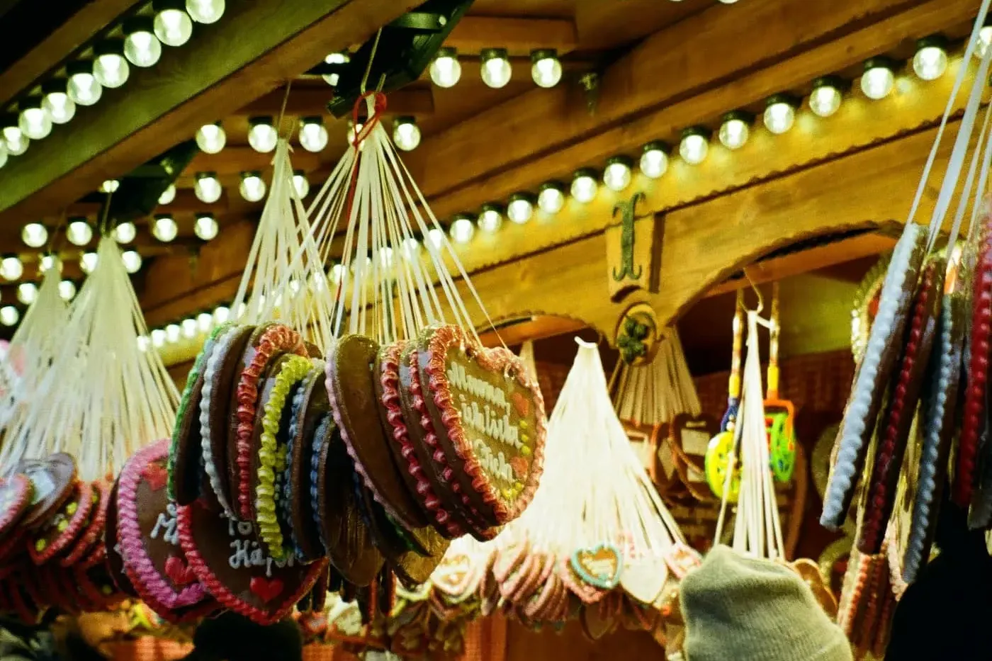 Hängende Lebkuchenherzen mit Zuckergussdekorationen und verschiedenen Süßigkeiten an einem festlichen Marktstand, mit Besu...