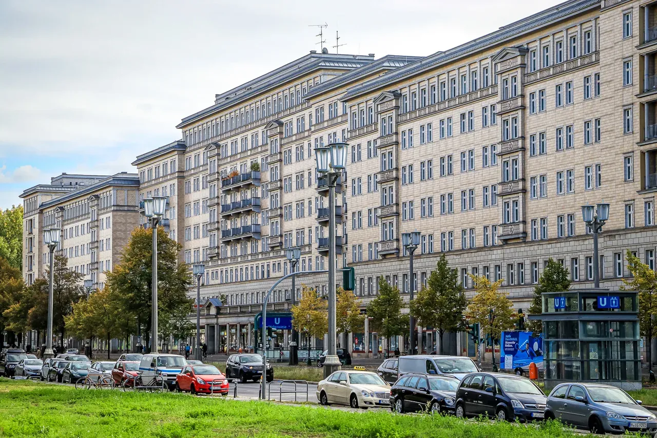 Grandes edificios de apartamentos de varios pisos con farolas, coches aparcados, árboles y una entrada de U-Bahn en Berlín.