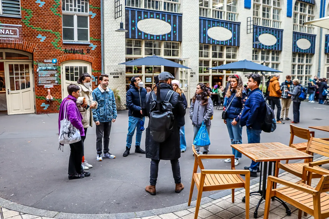 Ein Reiseführer mit Rucksack spricht mit einer Gruppe von Menschen im Innenhof der Hackeschen Höfe in Berlin.