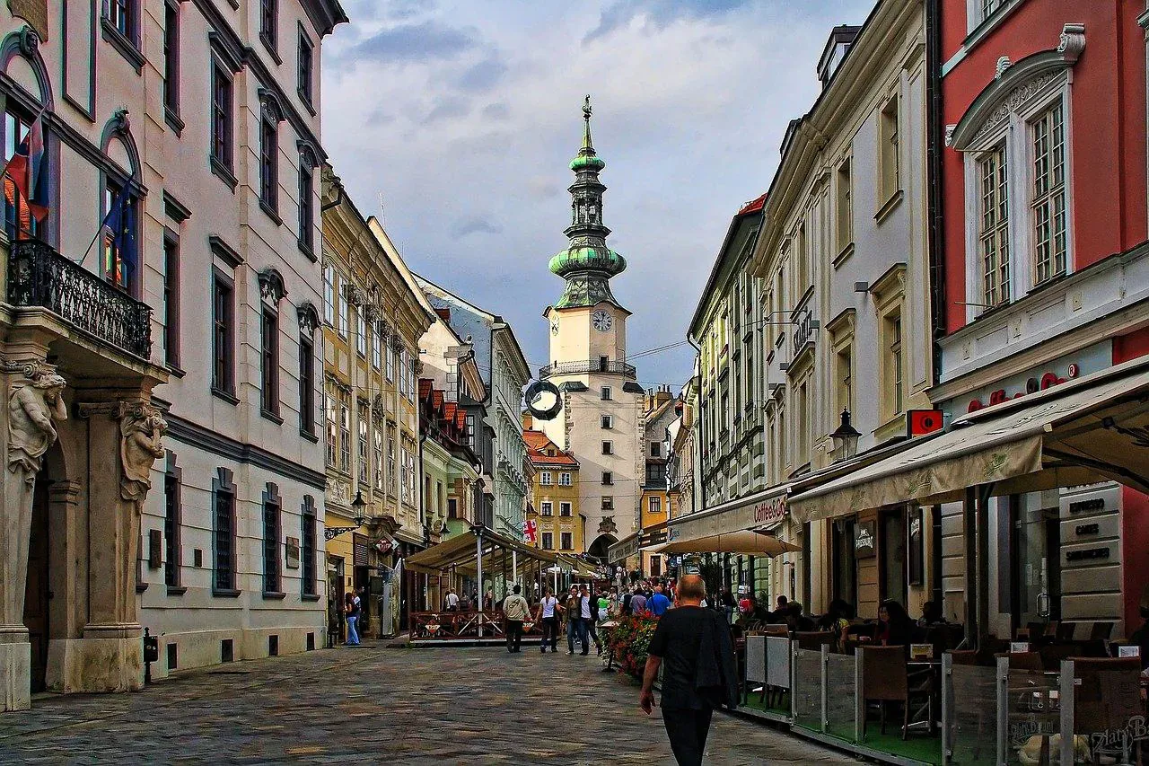 Calle histórica en Bratislava que conduce a la Puerta de San Miguel, flanqueada por edificios antiguos y cafés al aire lib...