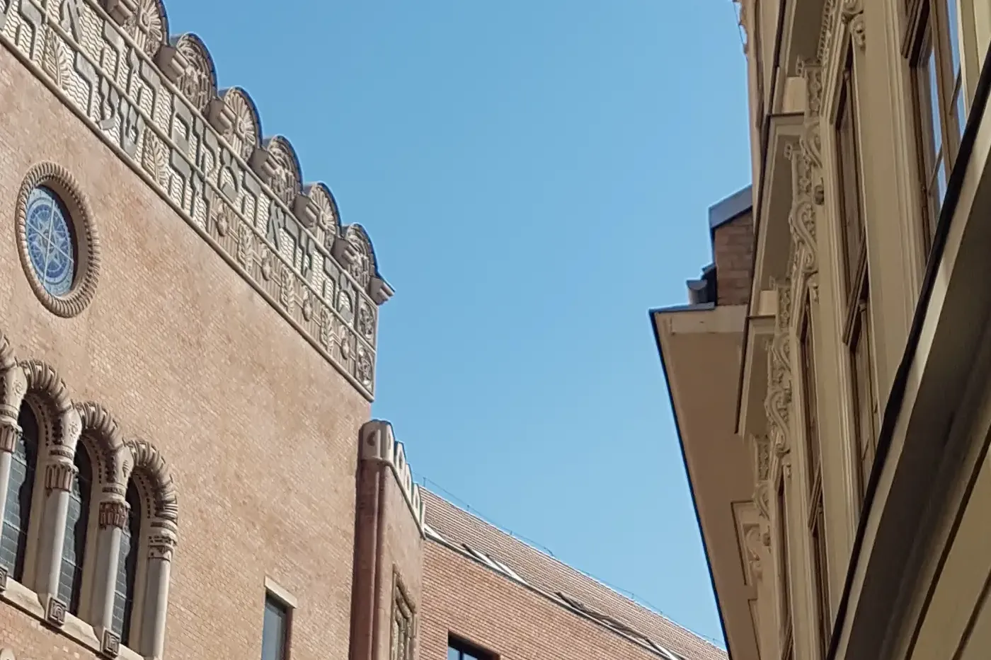 View of a Budapest street with brick buildings, one featuring Art Nouveau details and a round window, another with ornate ...