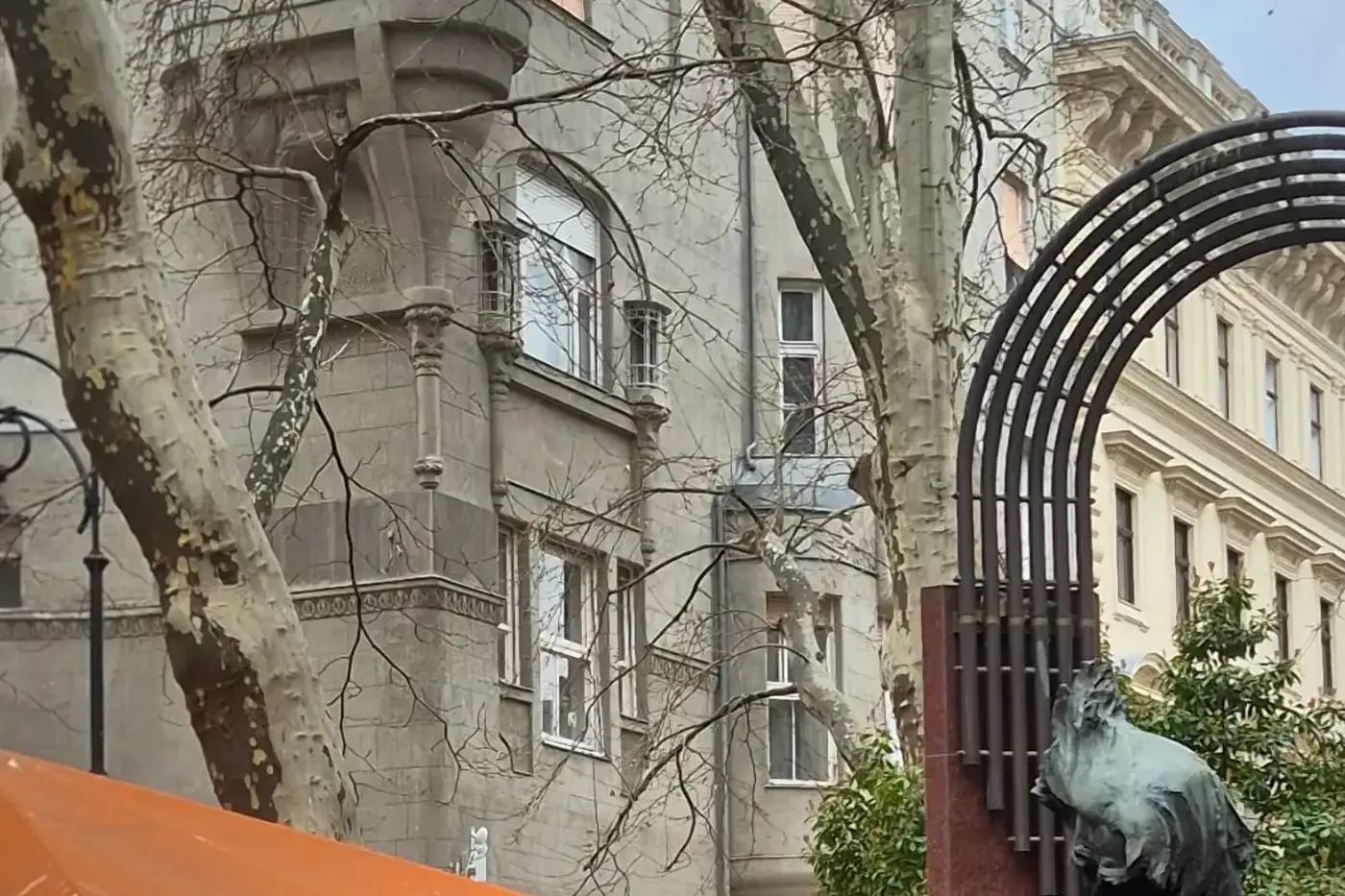 Bronze statue of Franz Liszt sitting, with bare trees, an orange cafe umbrella, and buildings in the background on a winte...