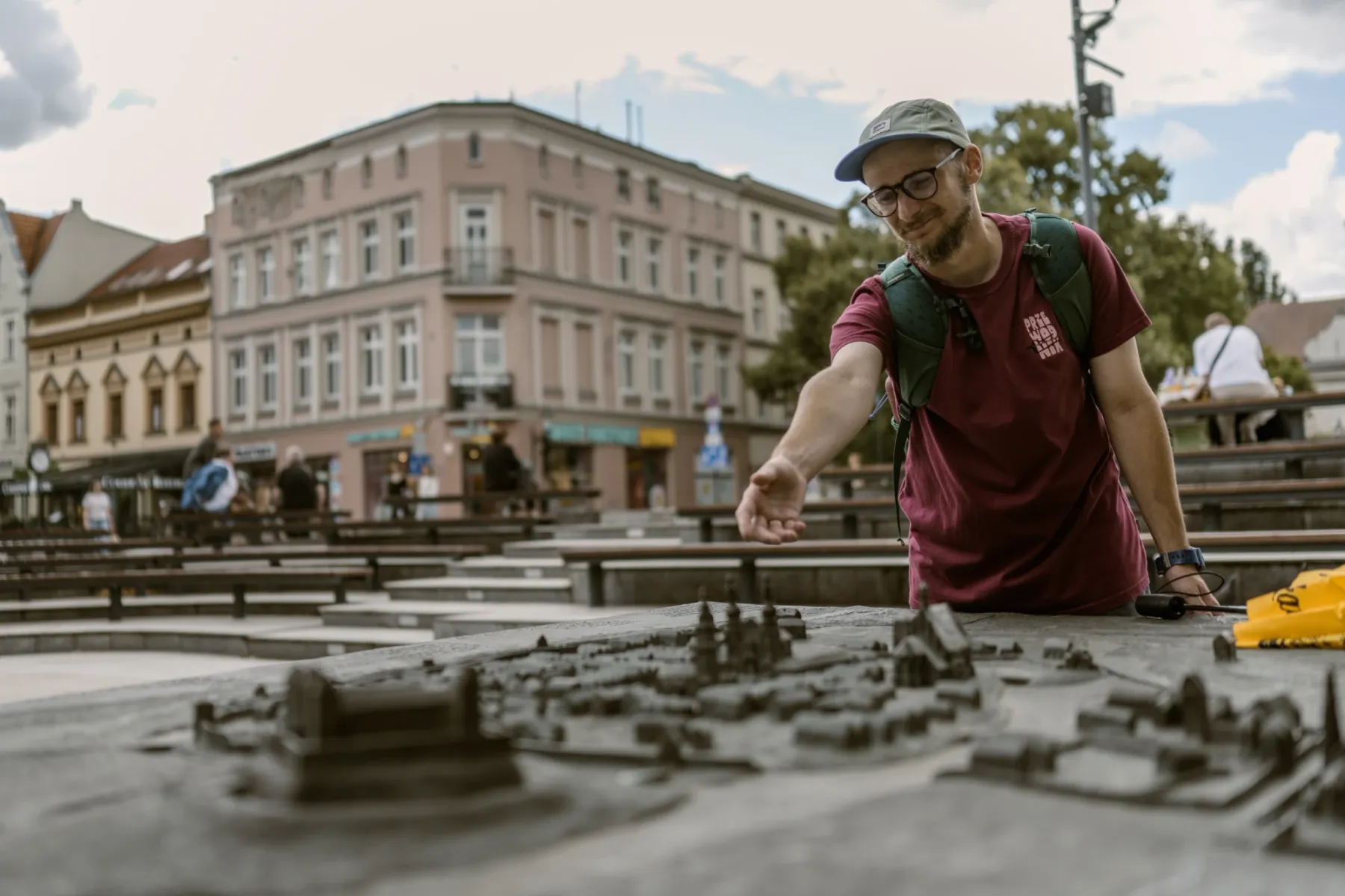 A man in a cap and glasses looks at a bronze model of the Old Town, with historic buildings in the background.