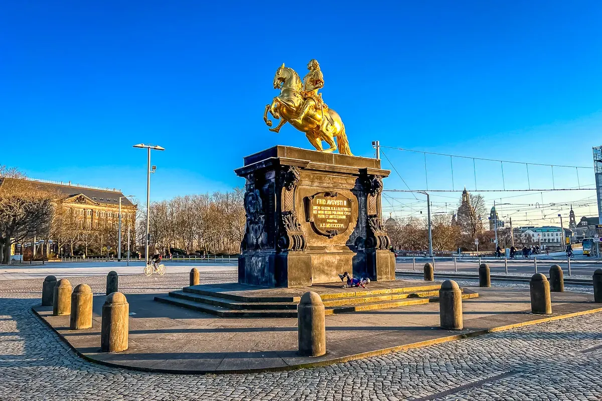 Golden equestrian statue of August the Strong on a dark pedestal in a cobblestone square, Dresden.