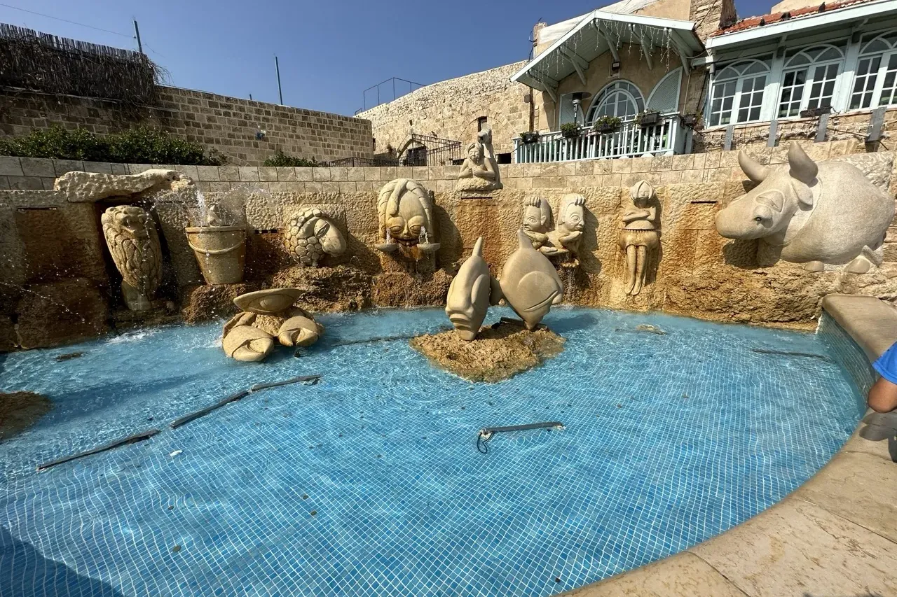 Fuente circular grande con agua de azulejos azules y un muro de piedra con diversas figuras talladas, incluyendo animales ...
