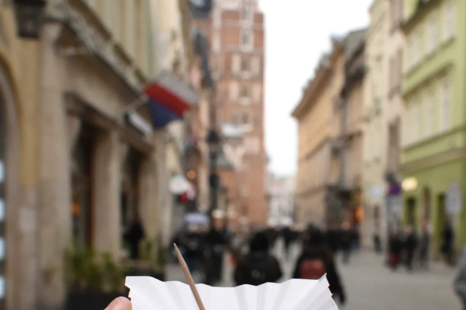 Hand holding grilled oscypek cheese with jam. St. Mary's Basilica in Kraków is blurred in the background.