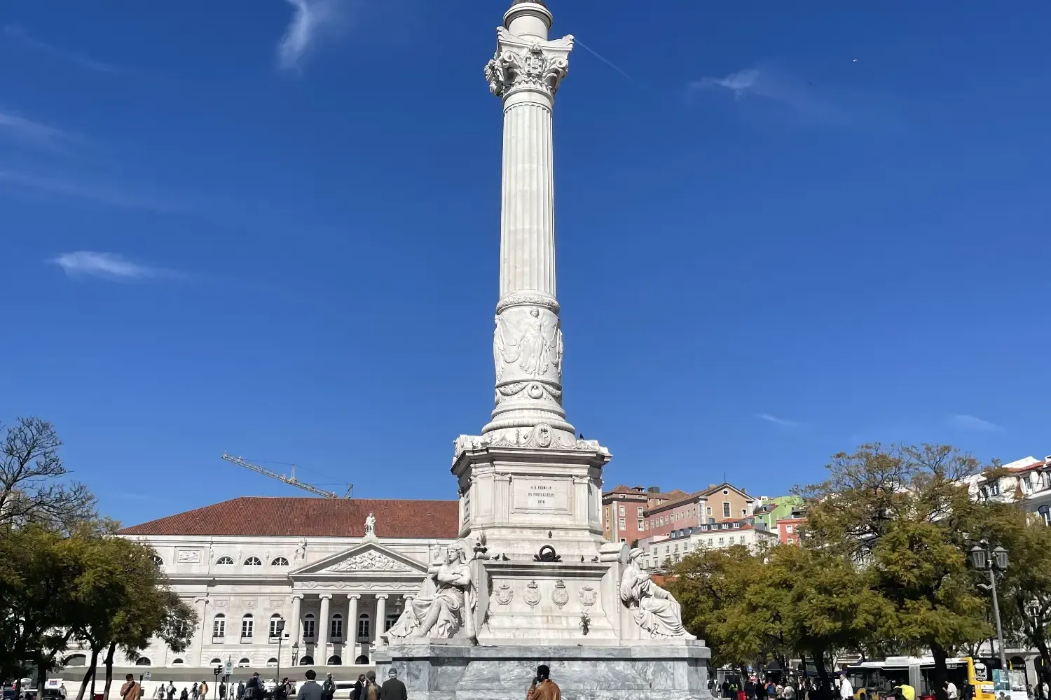 Rossio-Platz in Lissabon - Pedro-IV.-Denkmal, kunstvolles Wellenpflaster und historische Gebäude vor blauem Himmel.