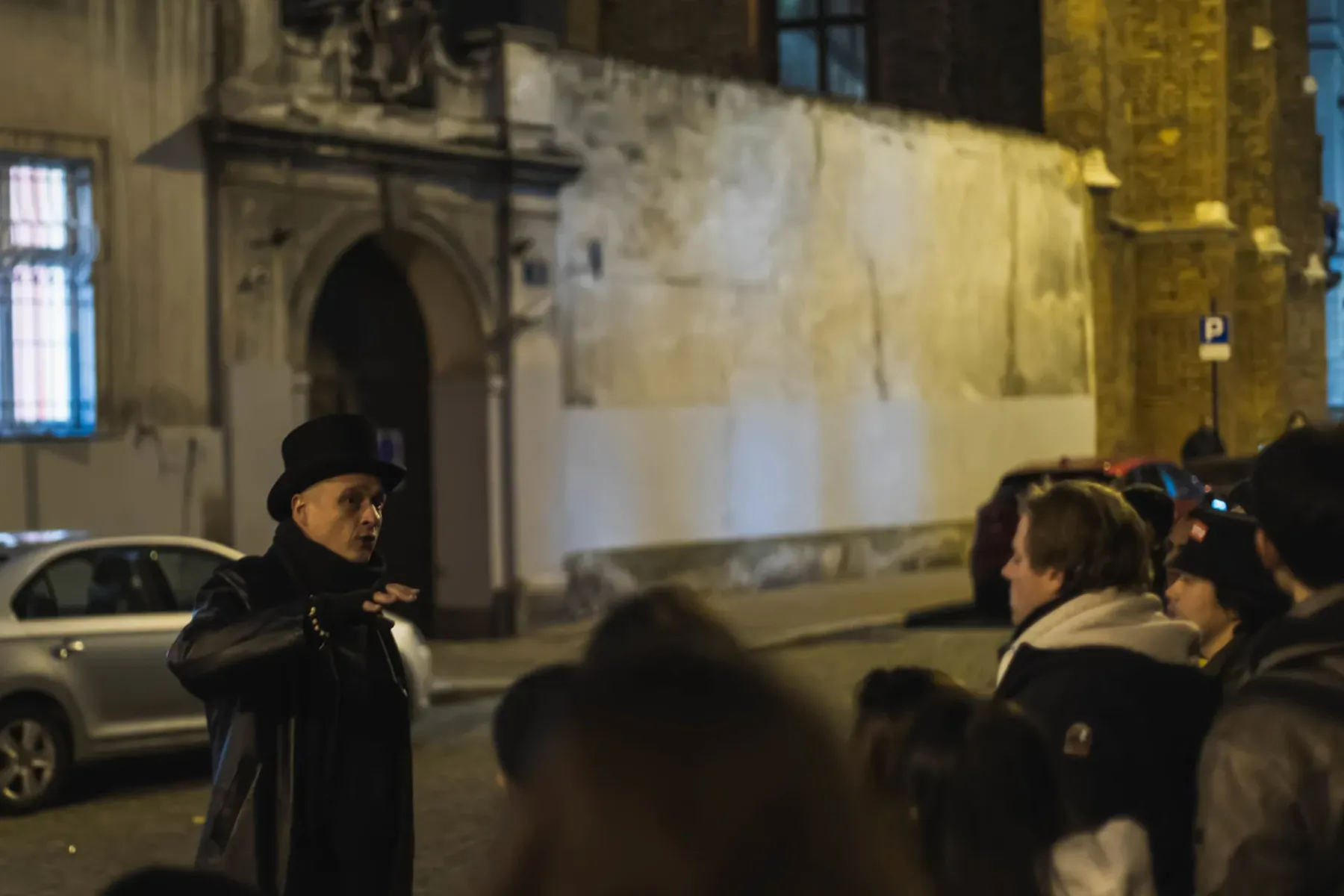 Reiseführer in Zylinder und Mantel spricht nachts mit einer Gruppe auf einer Kopfsteinpflasterstraße in Krakau. Historisch...