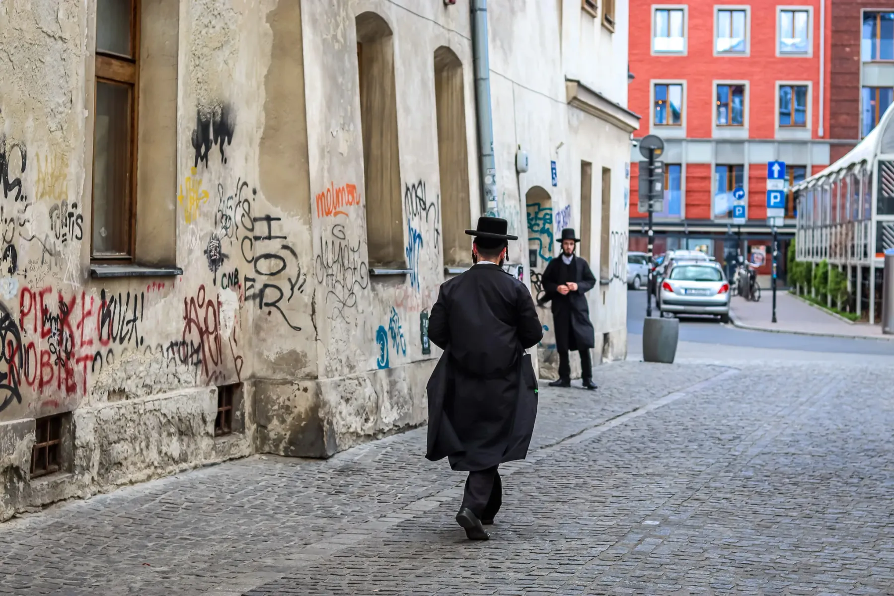 Dos hombres judíos ortodoxos en una calle adoquinada del barrio de Kazimierz de Cracovia, junto a un muro con grafitis.