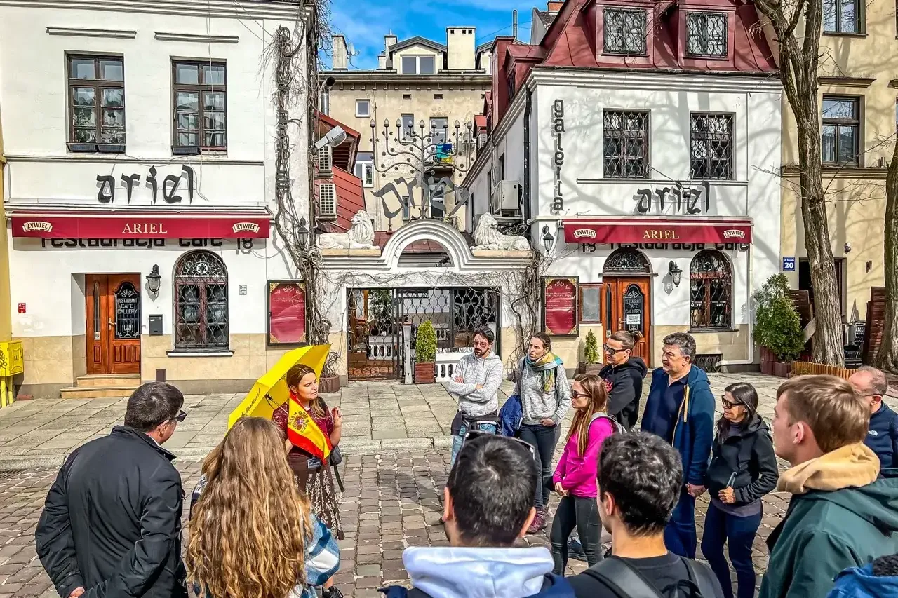Eine Reisegruppe hört einem Guide mit gelbem Schirm in der Szeroka-Straße im Krakauer Stadtteil Kazimierz zu.